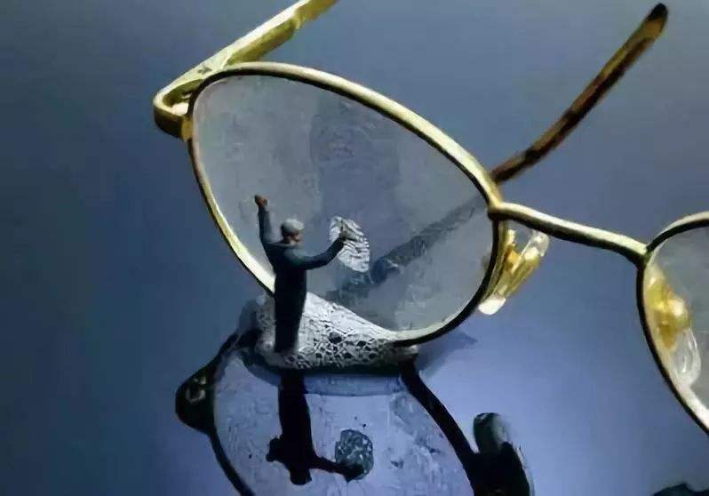 Miniature figure cleaning the lens of a pair of gold-rimmed eyeglasses